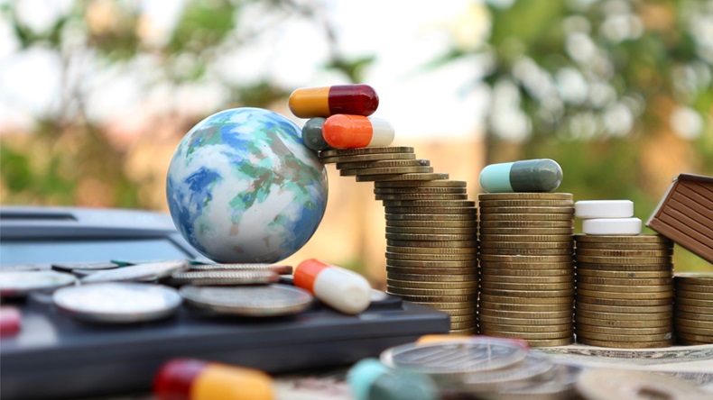 Miniature world globe on calculator and capsules on roll ladder of gold coin and pills medicine on money in blur natural tree bright light
