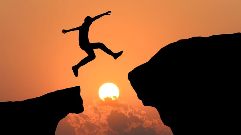 Silhouette of man jumping over cliff on sunset background , business concept 