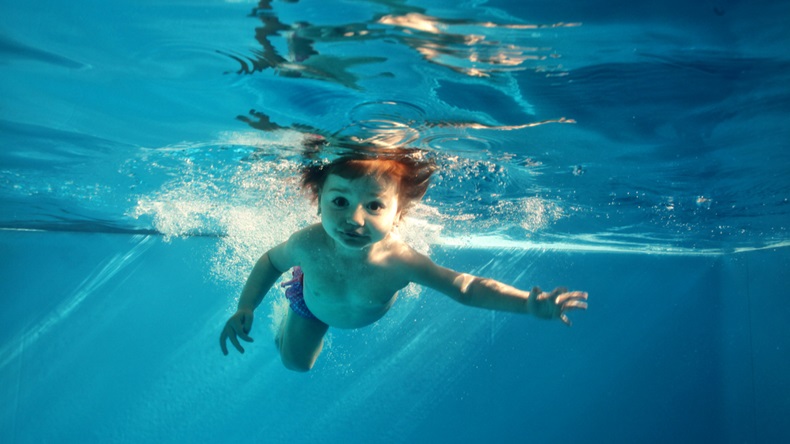 The little girl in the water park swimming underwater and smiling - Image 