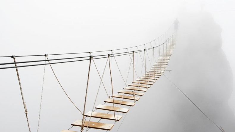 Fuzzy man walking on hanging bridge vanishing in fog. Focus on middle of bridge