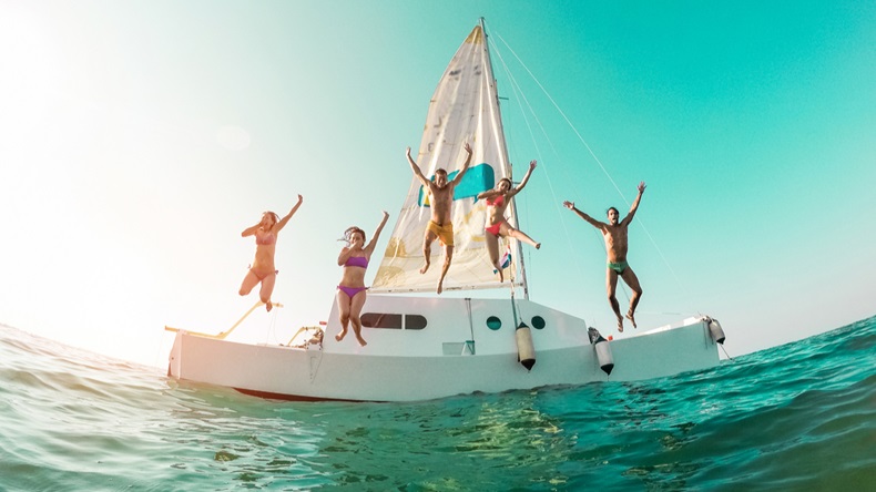 Happy crazy friends diving from sailing boat into the sea - Young people jumping inside ocean in summer vacation - Main focus on center guys - Travel and fun concept - Fisheye lens distortion