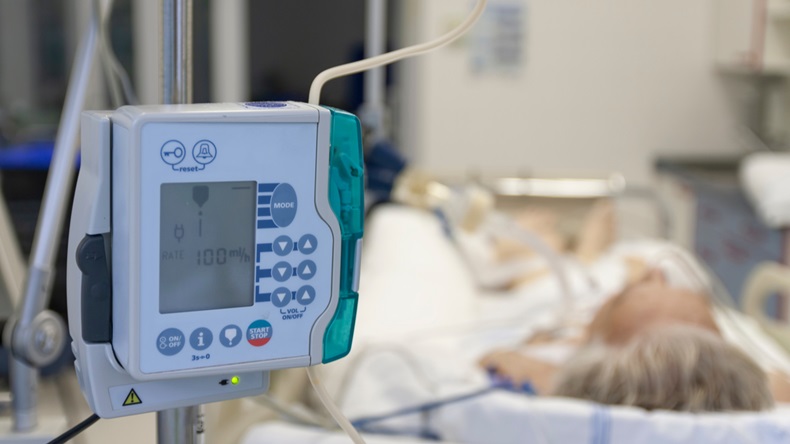 A small, lightweight, portable enteral feeding pump in ICU in hospital, on background patient in bed connected to medical ventilator in ICU in hospital
