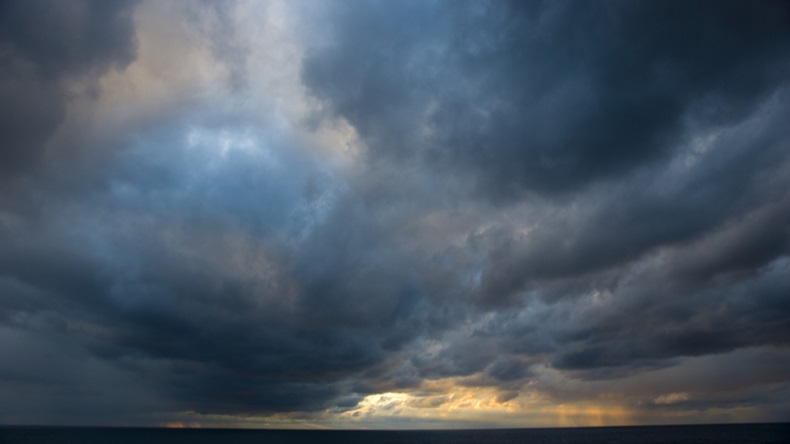 A huge storm cloud over the ocean with rays of sunlight poking through in at the horizon