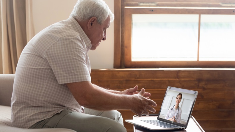 Elderly 70s man seated on sofa make distant video call, senior patient look at laptop screen communicating with doctor therapist online, older generation and modern tech application easy usage concept