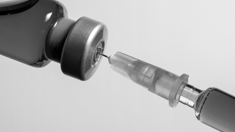 Needle pierces the cap of medical vial. Black and white macro photo.