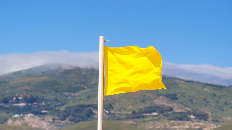 Yellow flag waving on the beach in the breeze against a blurred blue sky.