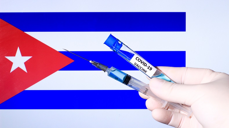 Hand in surgery glove holding syringe with covid vaccine. Cuban flag in the background
