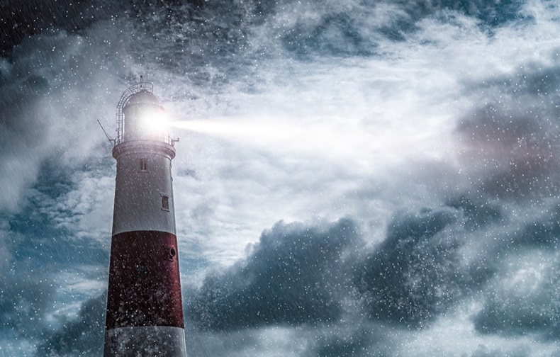 Large red and white lighthouse on a rain and storm filled night with a beam of light shining out to sea