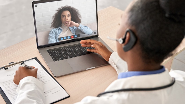 African doctor wear headset consult female black patient make online webcam video call on laptop screen. Telemedicine videoconference remote computer app virtual meeting. Over shoulder videocall view.