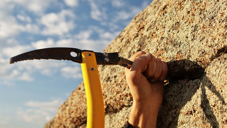 Hands rock-climber hammering in hook in rock. Alamy: D0TK5D