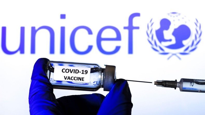 Hand on blue surgery glove extracting Covid vaccine from vial with a syringe. In the background Unicef organization
