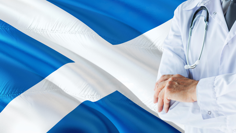 Scottish Doctor standing with stethoscope on Scotland flag background. National healthcare system concept, medical theme.