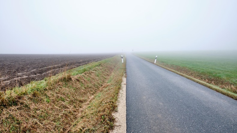 Winding countryside road to nowhere - narrow street with diminishing perspective leading into the fog. 