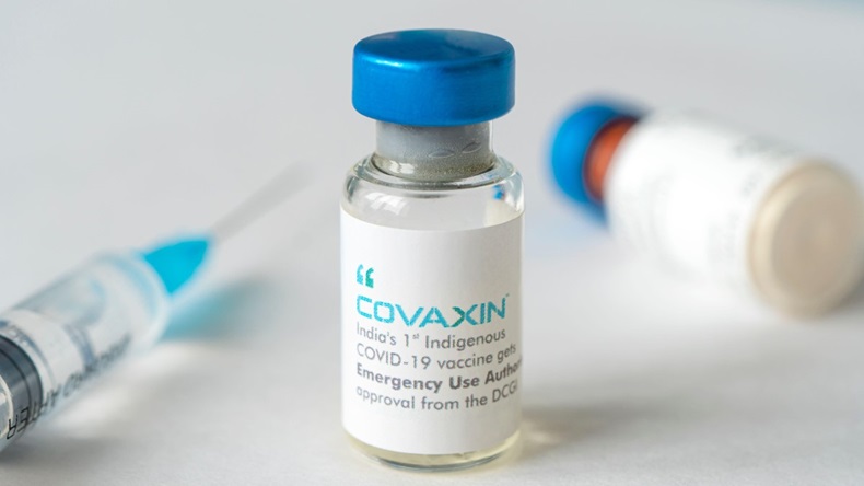 A bottle of vaccine and a syringe on a white table on a blue background