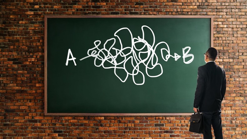 Businessman looking and thinkin front of a chalkboard brick wall with the complicated solution from point A to point B