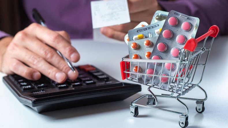 Concept of large spending on medicines. Shopping cart full of medicines and pills. A man calculates the cost of medicines on a calculator holding a check in his hand.