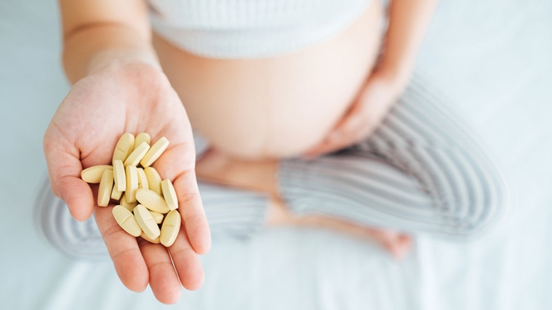 Belly of pregnant woman and vitamin pills in the hand.,Close-up.