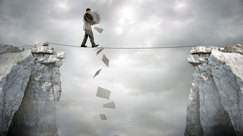 Business Balance - A businessman carrying paperwork walking over a tight rope.