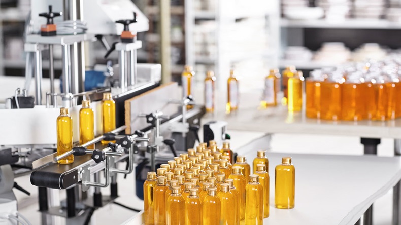 Bottles filled with yellow thick substance standing on desk and conveyor line. Production line of cosmetics products on big factory. Automated process of creation shampoo on factory.Research concept