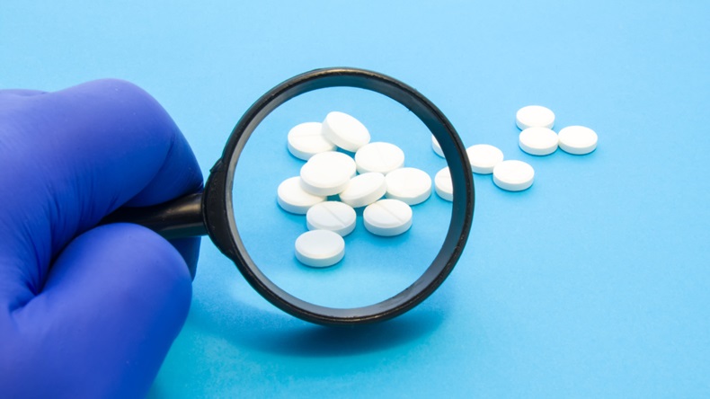 Pharmaceutical inspection of pills with magnifying glass.   Pharmacist or expert on pharmaceutical inspection identifies pills. Testing, verification and determining pharmaceutical counterfeiting or fakes of medicines and medicinal substance quality concept (iStock / Getty Images Plus)
