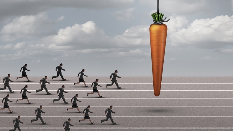 incentive business concept as a group of businessmen and businesswomen run on a track towards a dangling carrot on a moving cable