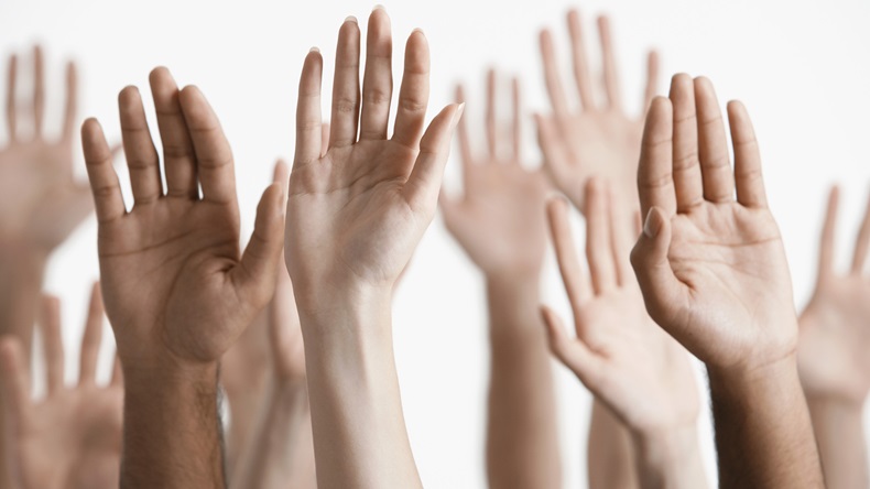 Closeup of multiethnic men and women raising hands against white background. Shutterstock-144918361