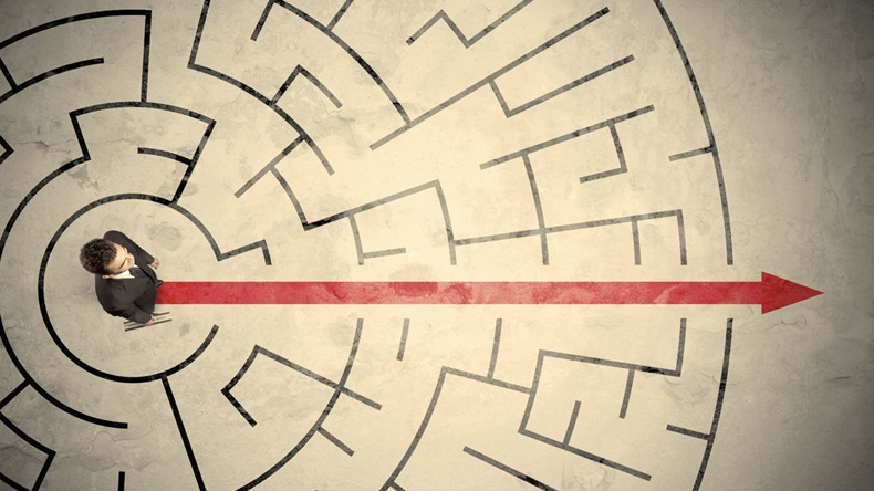 Business person standing in the middle of a circular maze with red arrow