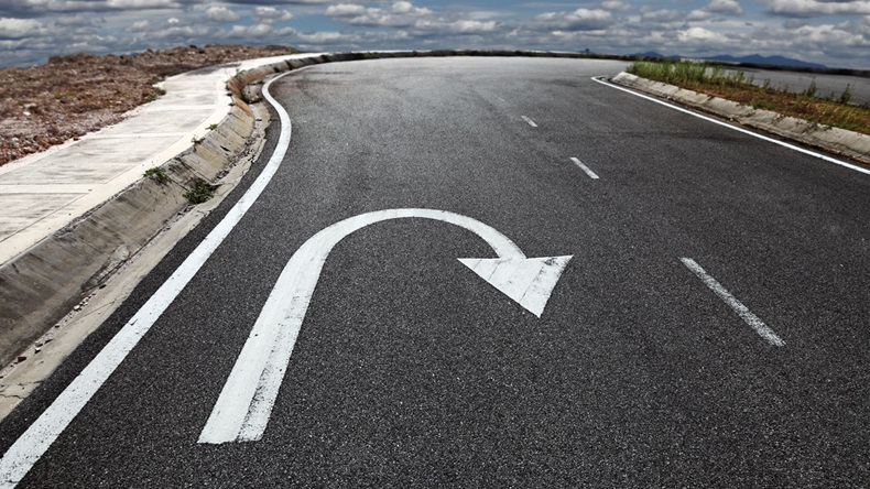 A U turn arrow traffic symbol imprint on a lonely asphalt road against a blue cloudy sky. - Image