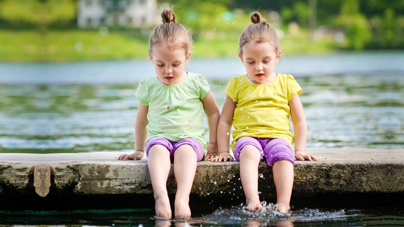 Twin girls are exercising on a lake shore, sprinkling water.