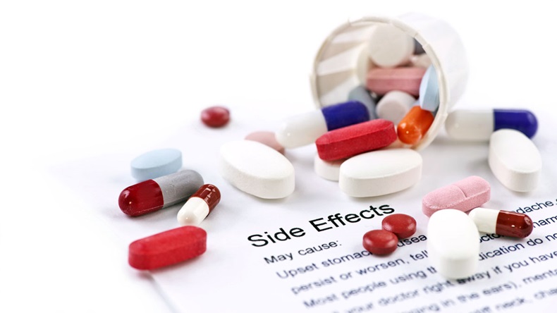 Assorted pills and capsules with side effects information sheet.
